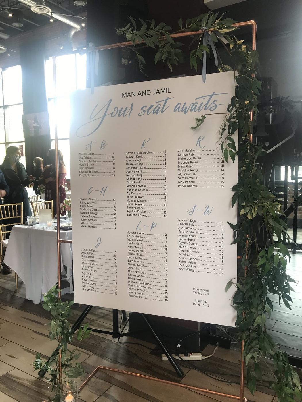 Large seating chart list with guest names organized alphabetically, framed in greenery