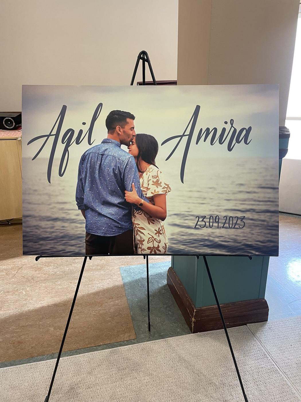 Engagement sign with names and date, hand-lettered in script over a beach photo