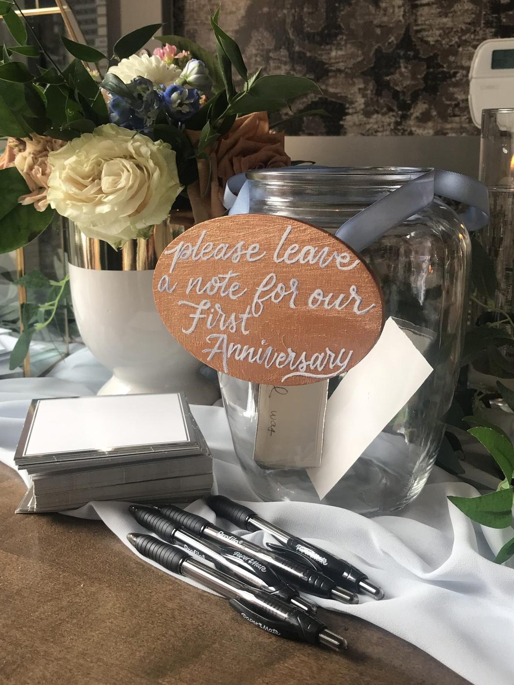 Hand-lettered wooden sign inviting guests to leave a note for a first anniversary